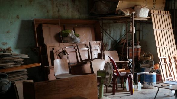 A cluttered workshop filled with wooden furniture, tools, and various items in natural lighting.