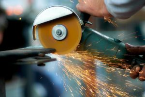 Crop anonymous craftsman using angle grinder to cut metal details while working in workshop